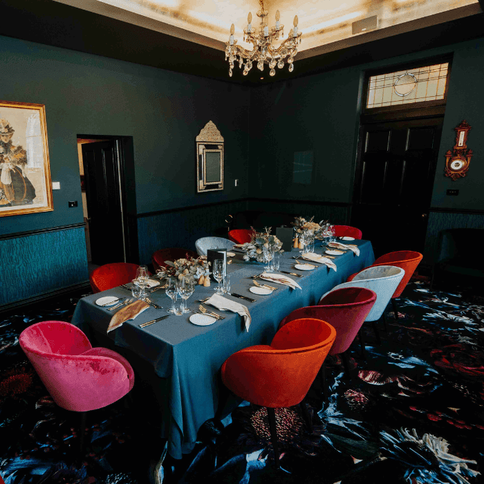 Elegant dining room with a long table, colorful chairs, and a sparkling chandelier.