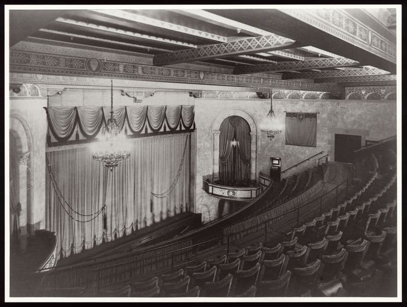 Ornate vintage theater interior with rows of empty seats and a grand stage.