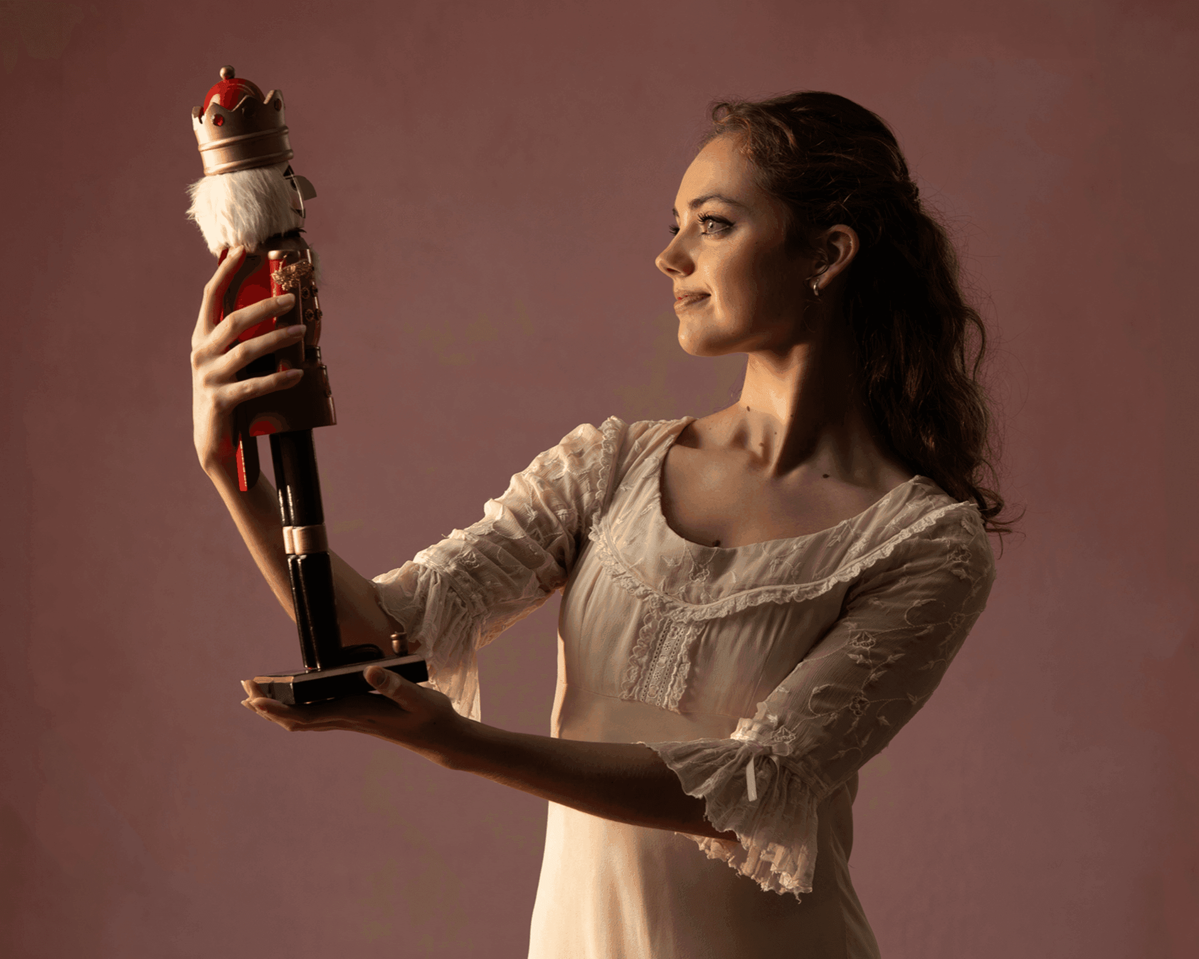 A woman in a white dress gently holds a Nutcracker doll, gazing at it thoughtfully.