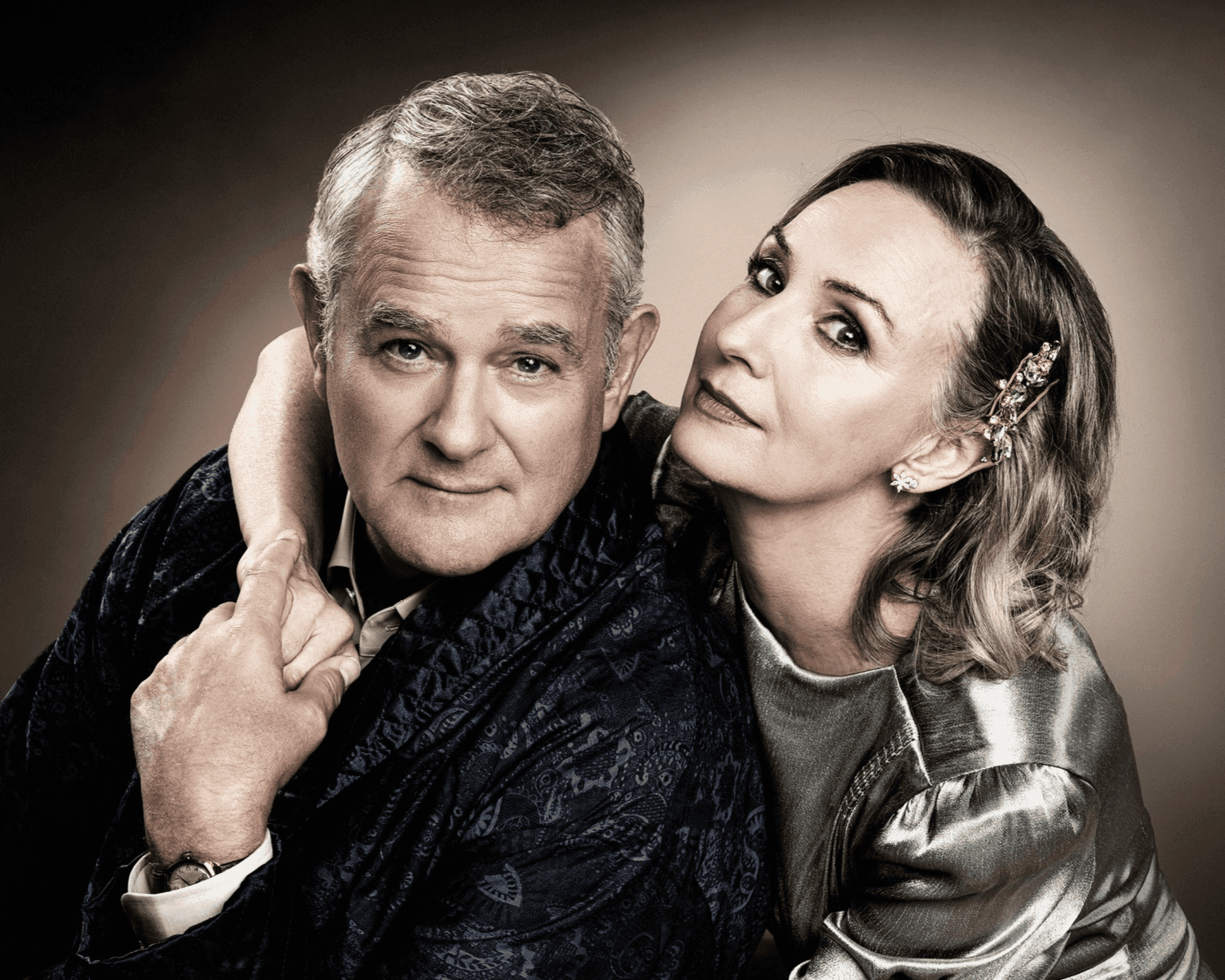 A man in a patterned robe and a woman in a silver dress pose intimately for a portrait.