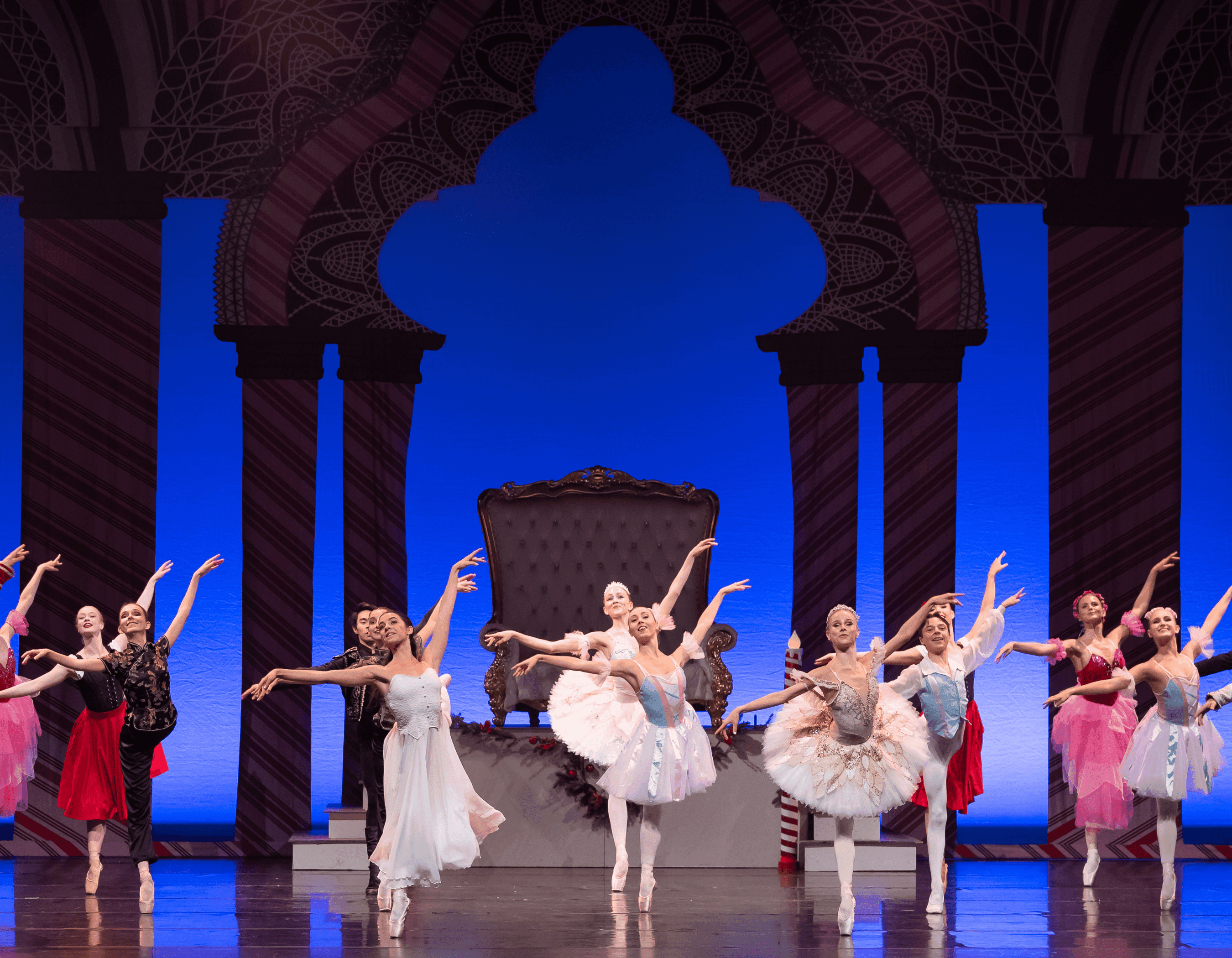 Ballet dancers in colorful costumes perform on an ornate stage with a blue backdrop.