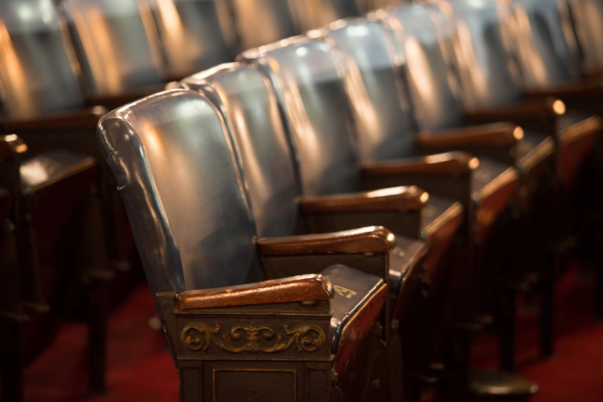 Row of vintage dark leather chairs with wooden arms in a dimly lit auditorium.