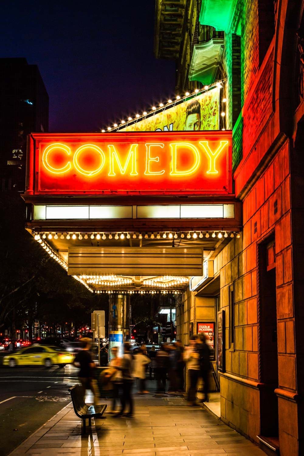 Bright red neon sign spelling 'COMEDY' illuminates a theater at night.