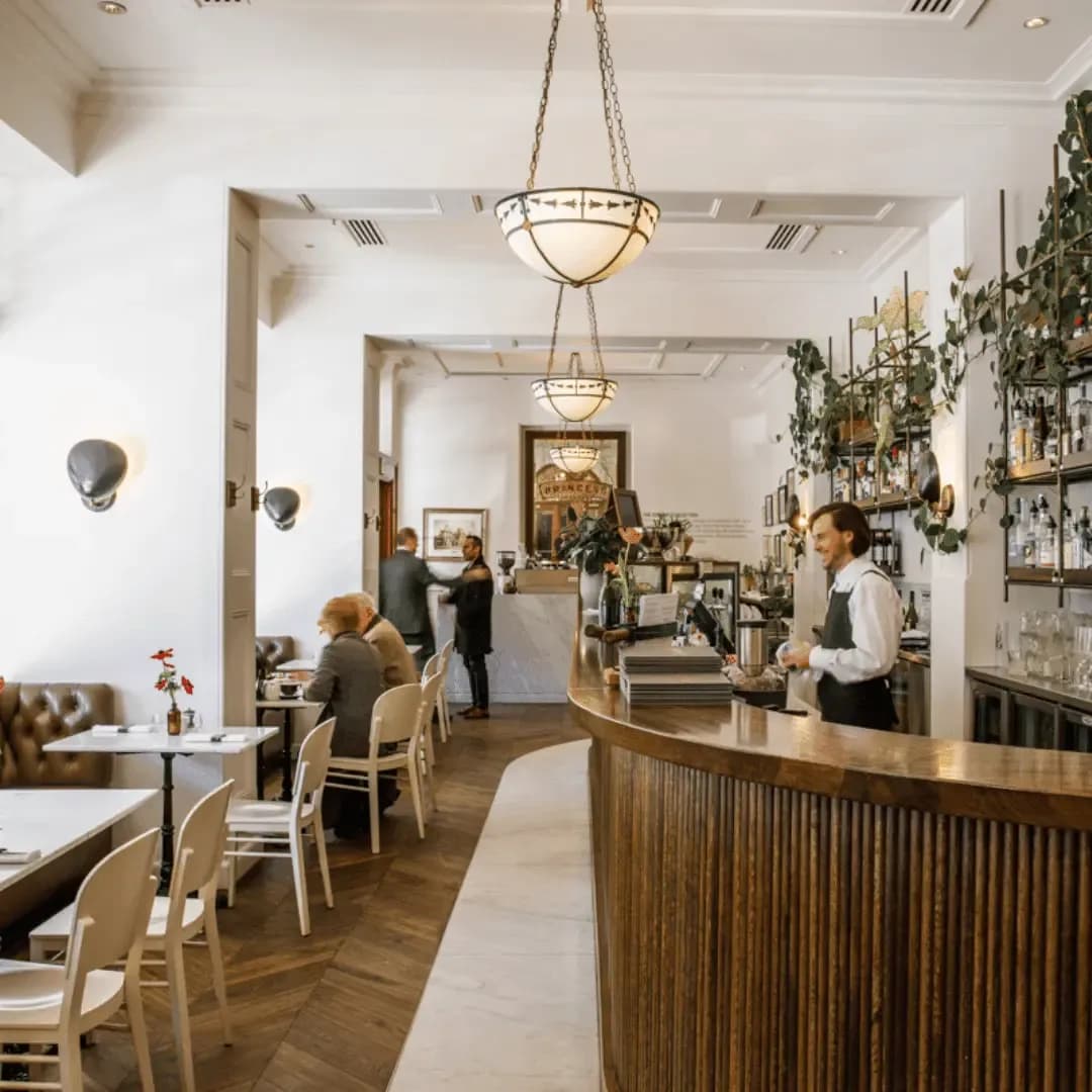 Elegant cafe interior with a wooden bar, hanging lamps, and patrons enjoying drinks.