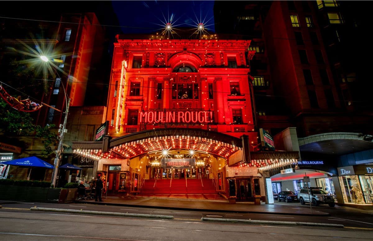 Red-lit Moulin Rouge theatre building at night with bright marquee lights and street.