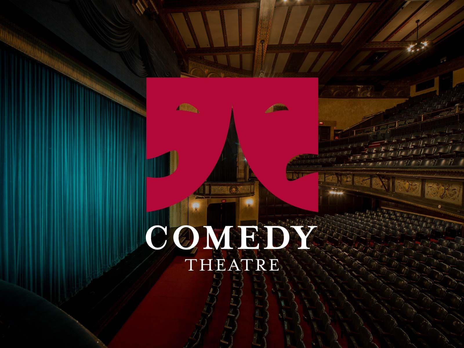 Theater interior with rows of seats, blue curtain, and a red Comedy Theatre logo.