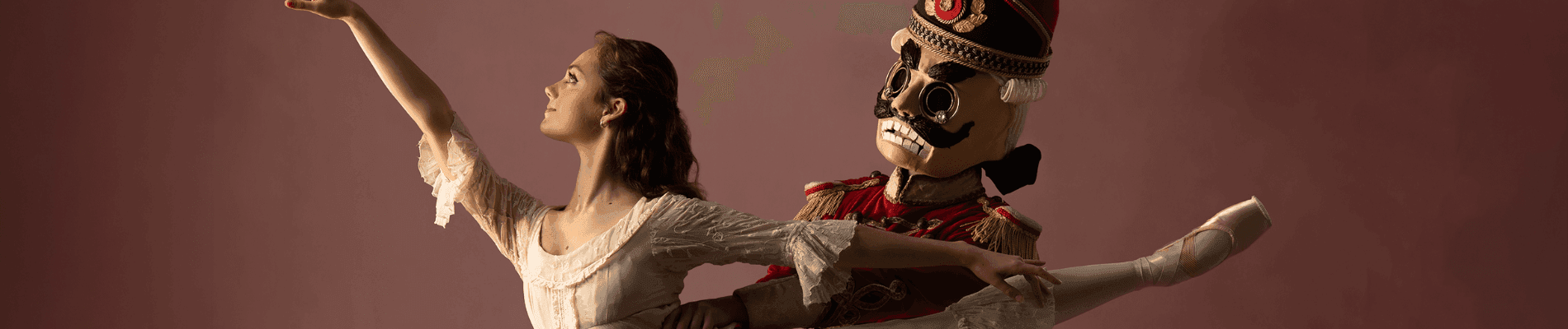 Ballerina in a white dress poses gracefully next to a Nutcracker doll.