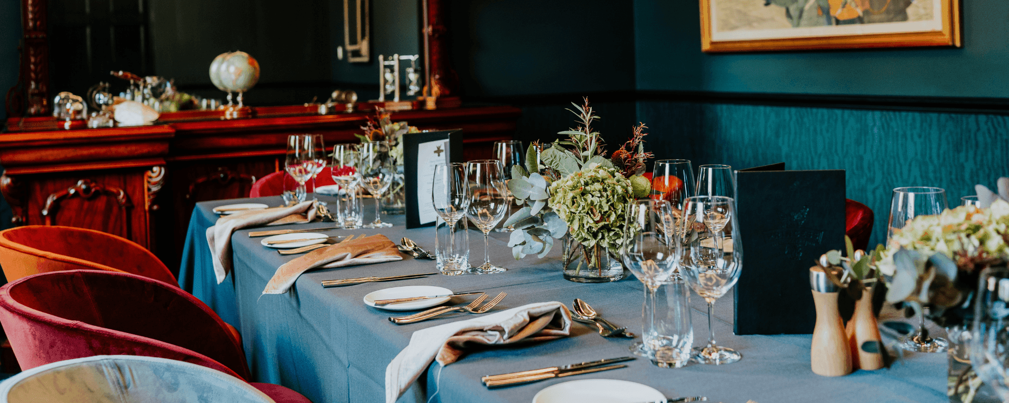 Elegantly set dining table with floral centerpieces, crystal glasses, and colorful chairs in a refined restaurant.