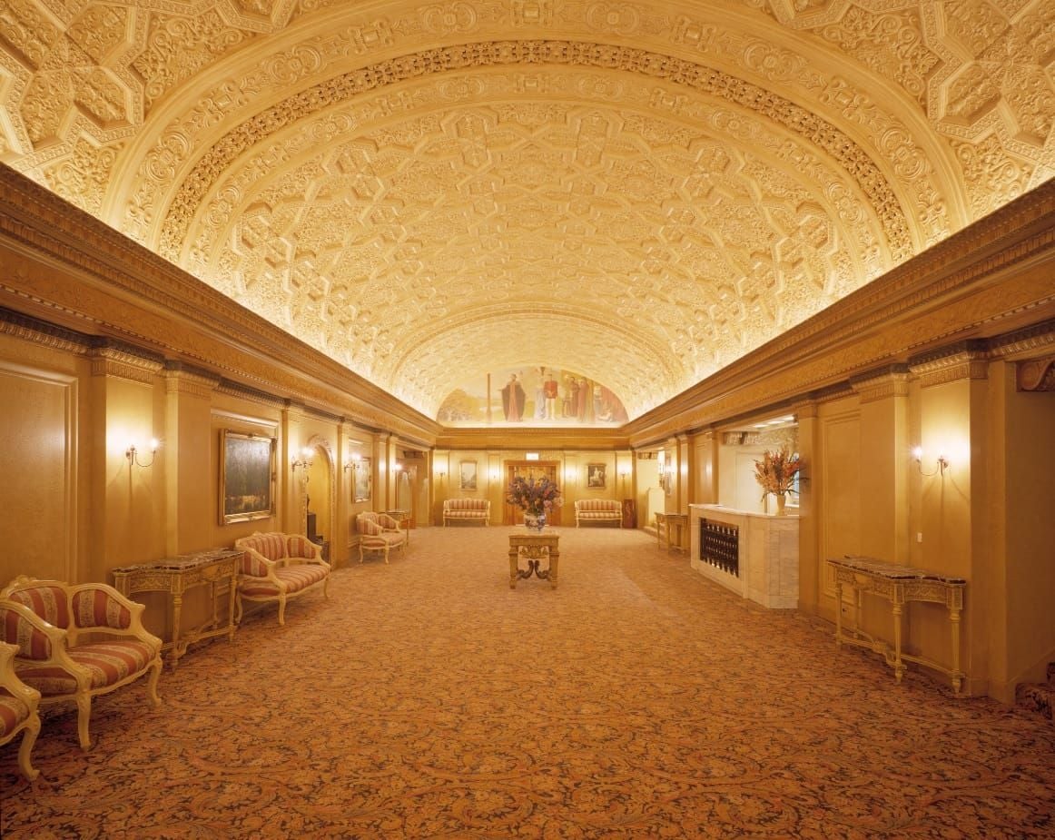 Luxurious grand hall with ornate arched ceiling, golden walls, and lounge seating.