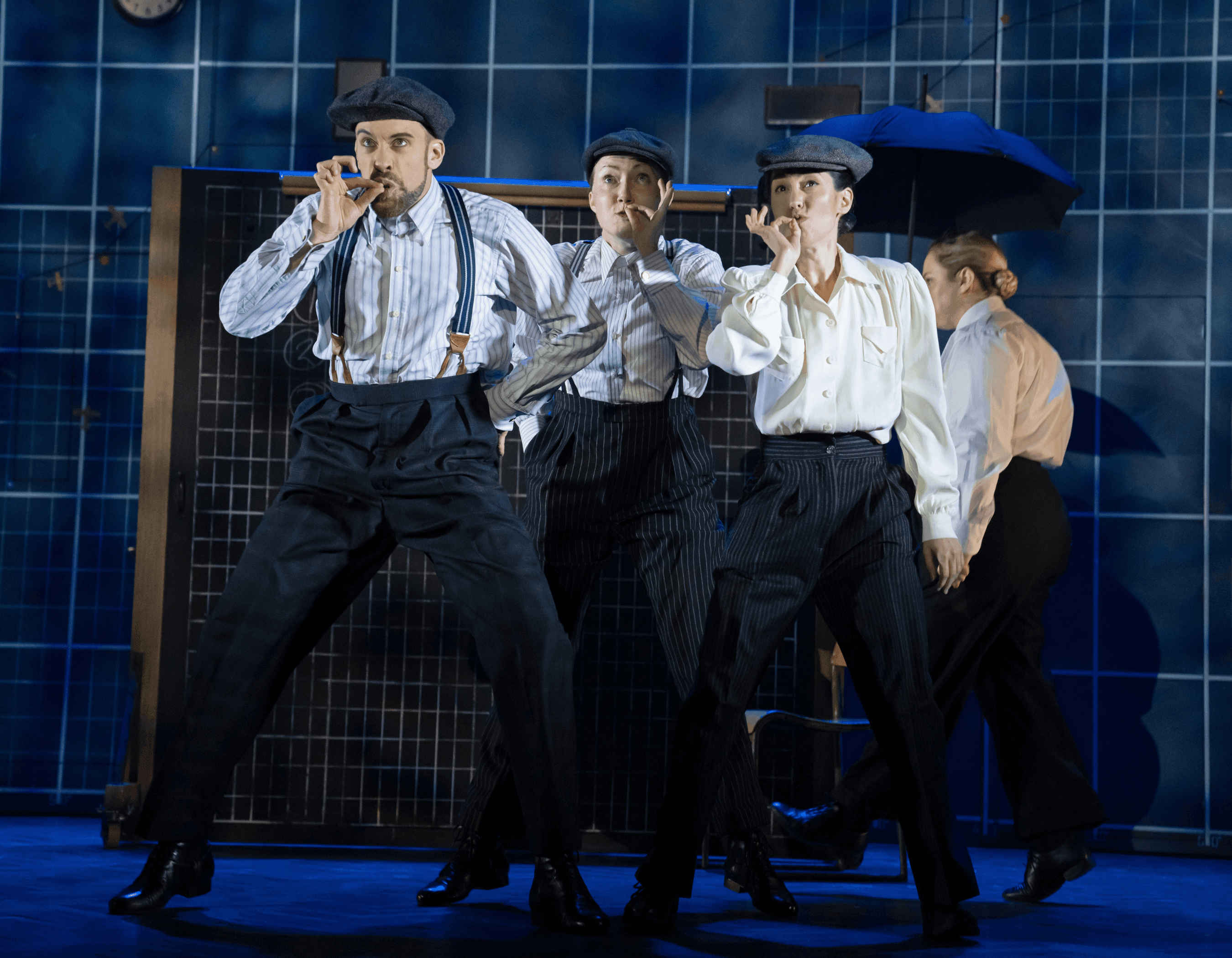 Three performers in vintage attire, with flat caps and suspenders, dancing on a stage.