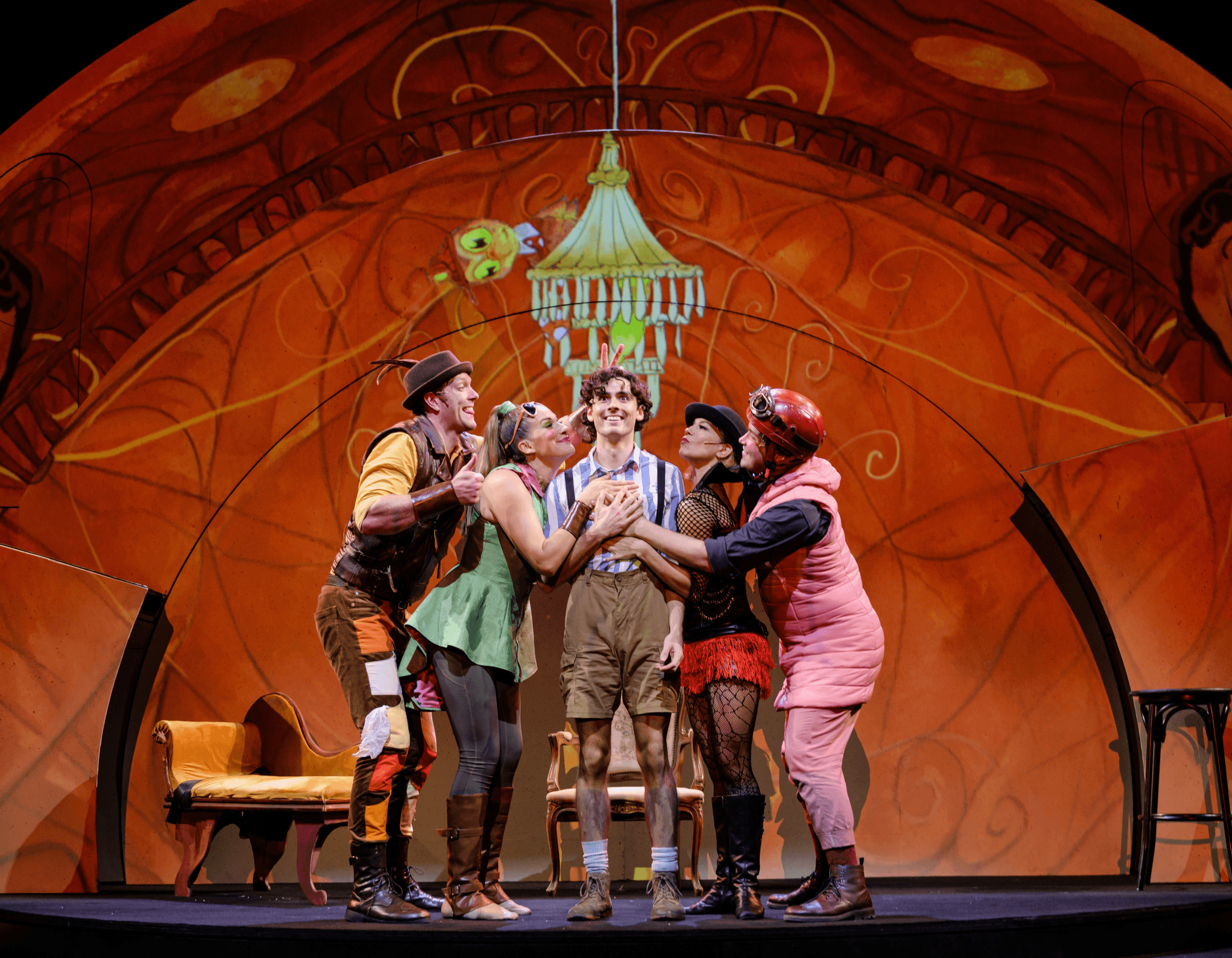 A young actor is celebrated by four other performers on a vibrant theatrical stage.