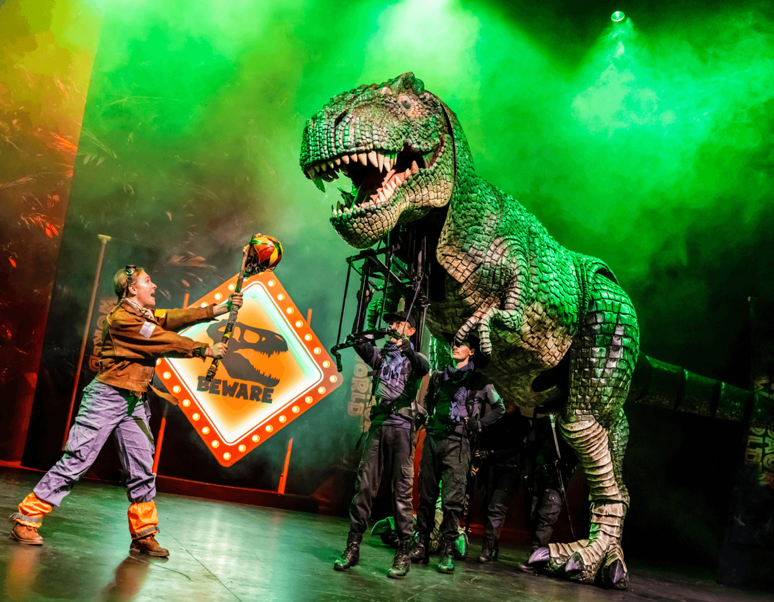 Giant T-Rex puppet on stage, with a person holding a 'BEWARE' sign.