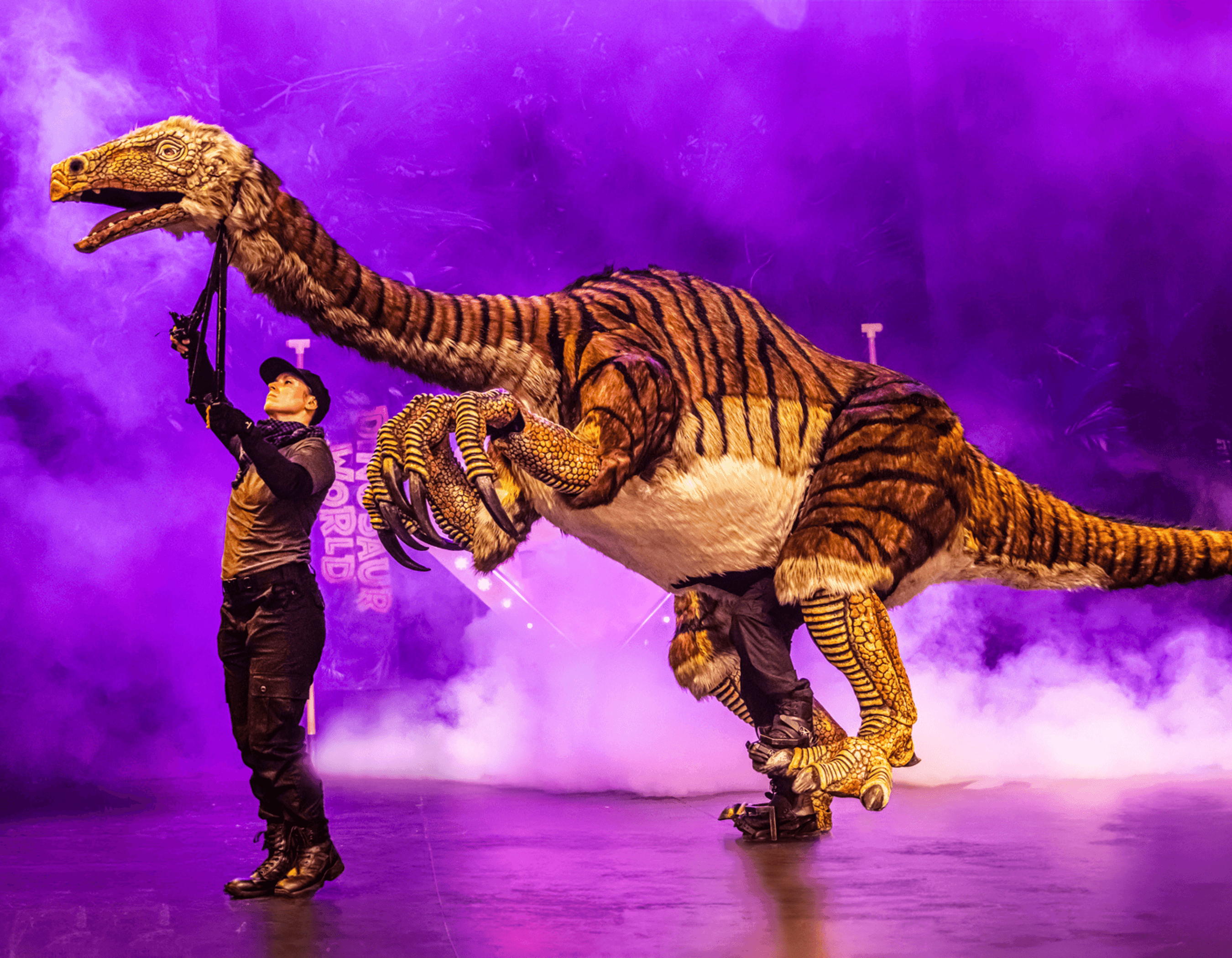 A puppeteer operates a large dinosaur puppet on a smoky stage with purple lighting.