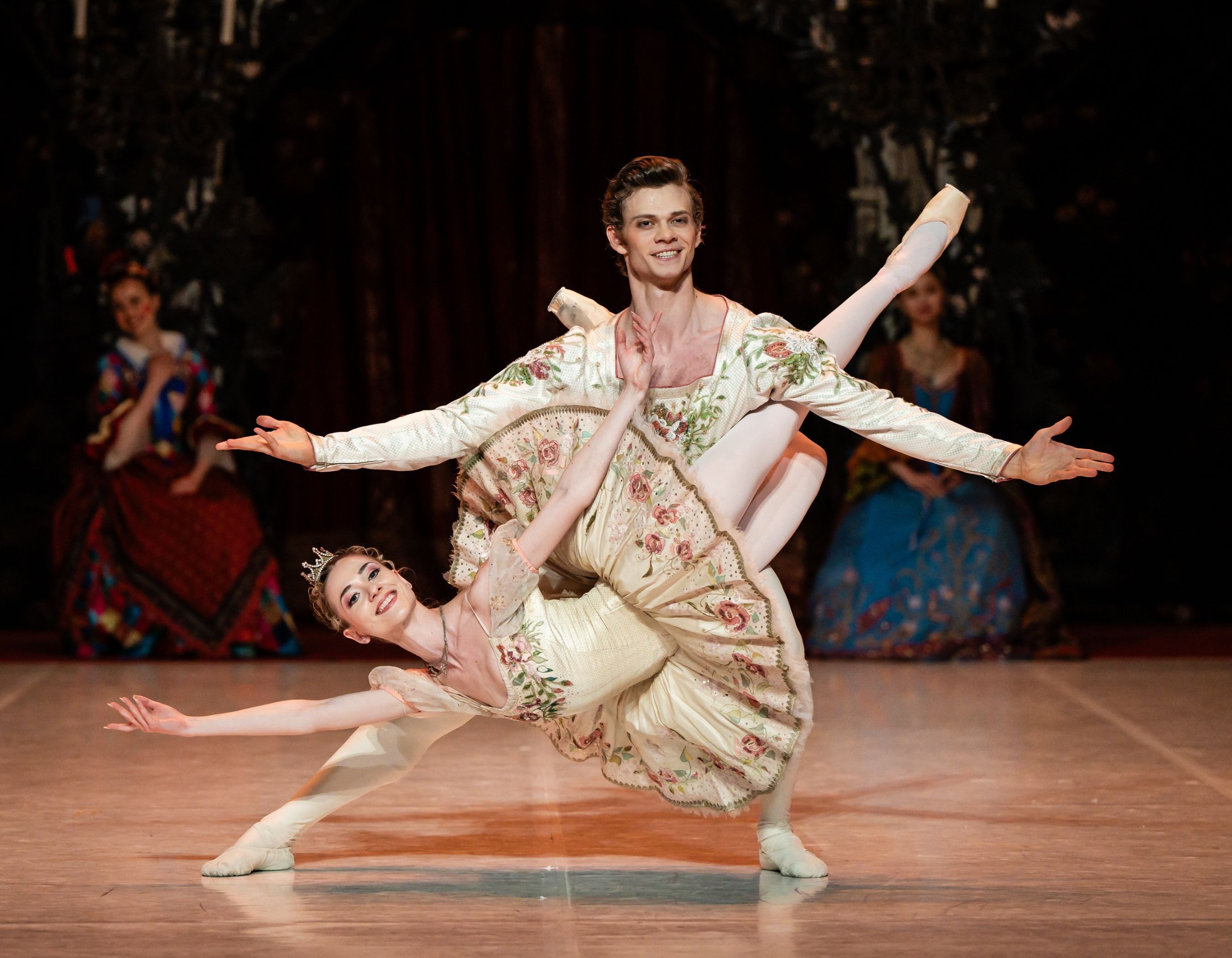 Two ballet dancers in ornate costumes perform a graceful pose on a stage.