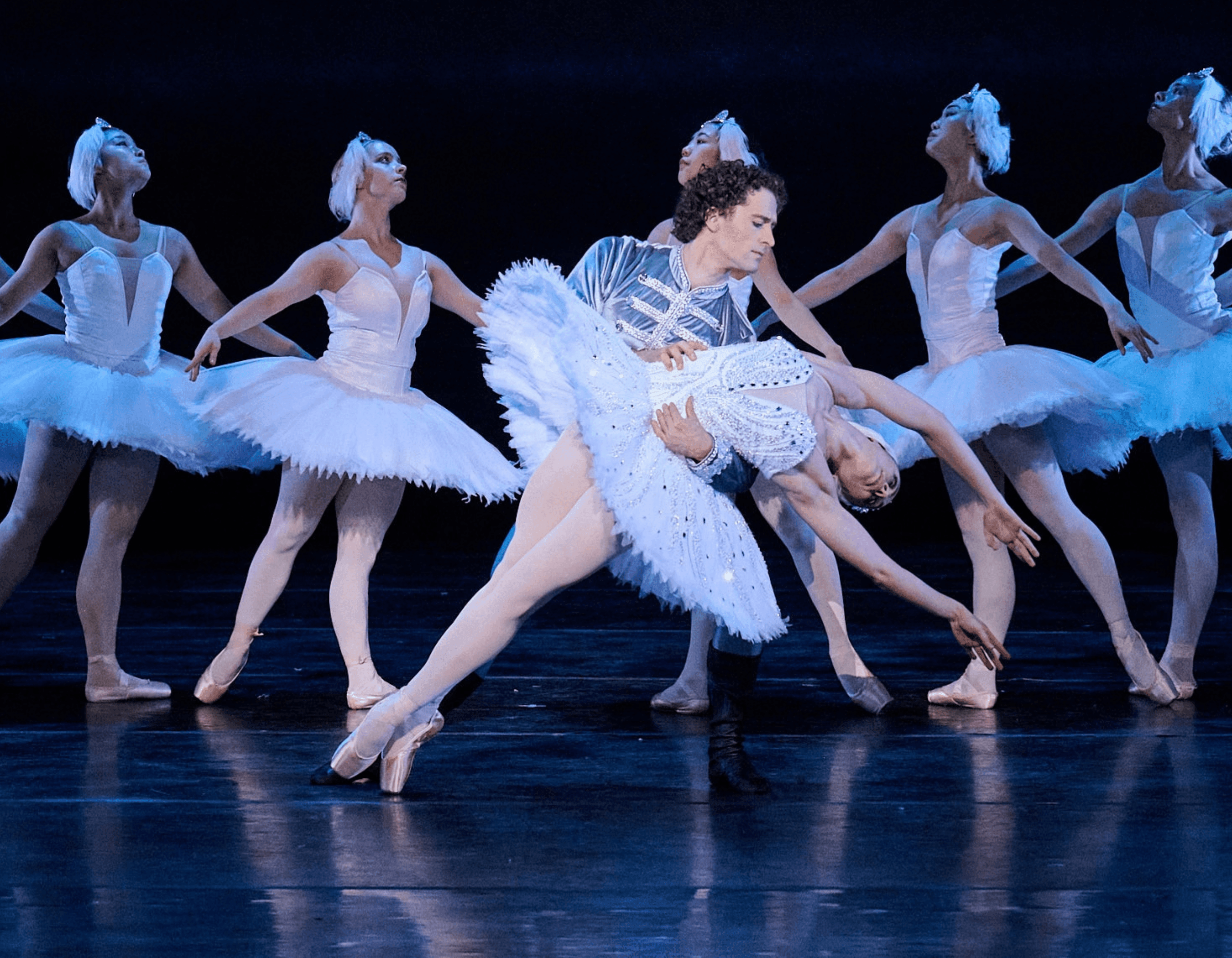 Two lead ballet dancers in a dramatic pose, supported by other dancers in white tutus.