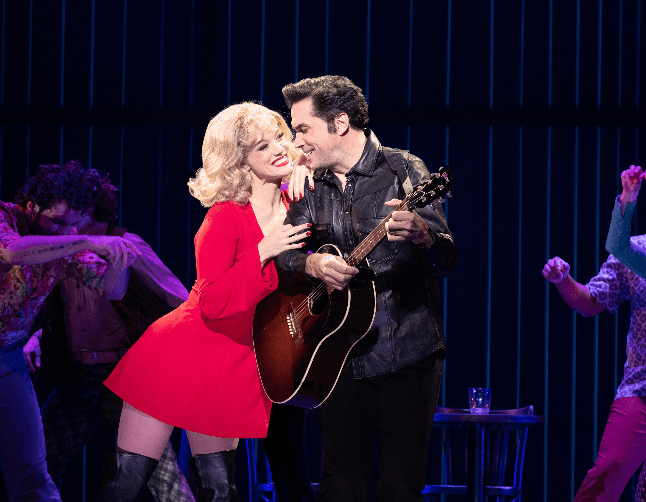 A woman in a red dress and a man with a guitar perform intimately on stage.