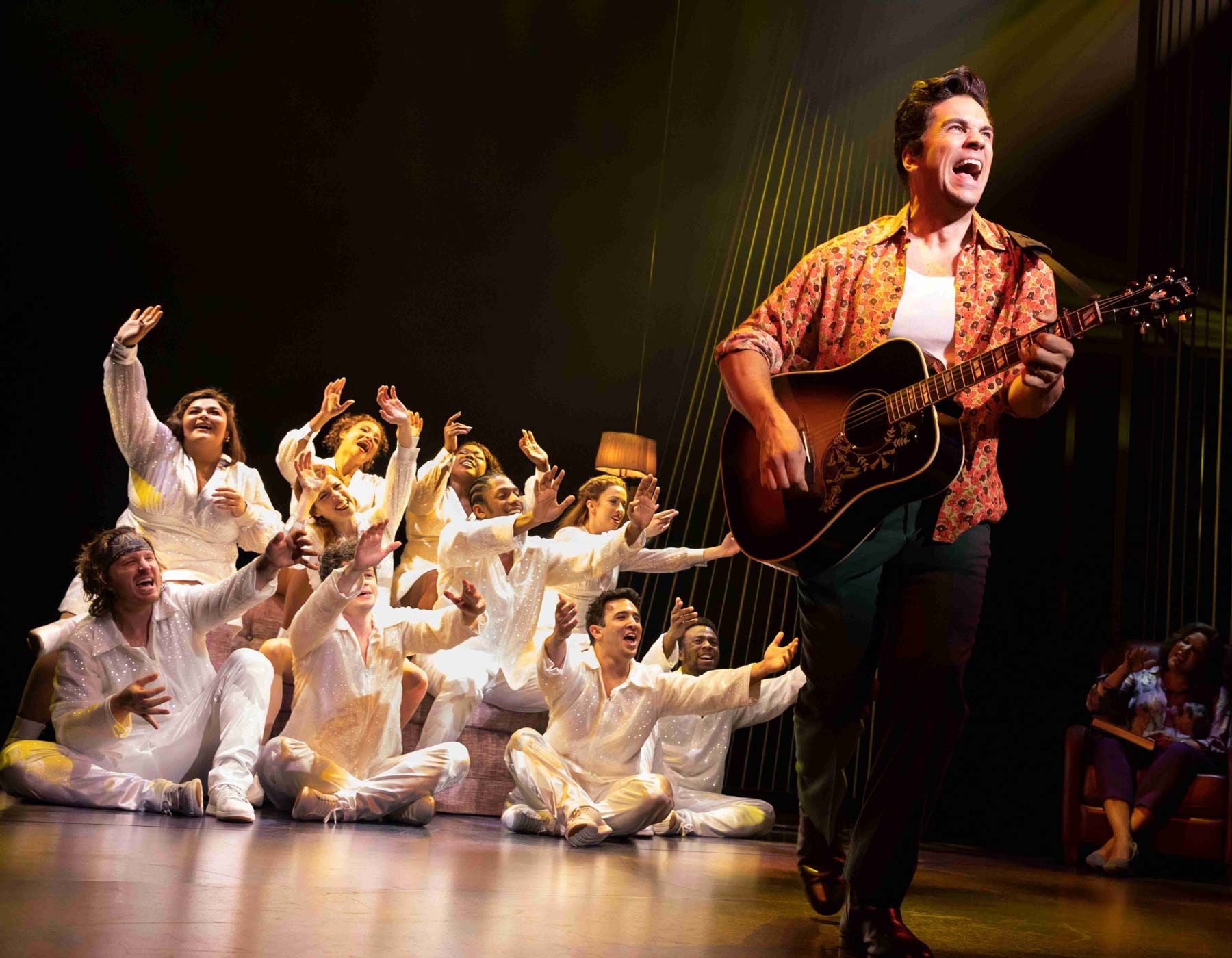 Singer with guitar performs on stage while a chorus of people raise their hands.