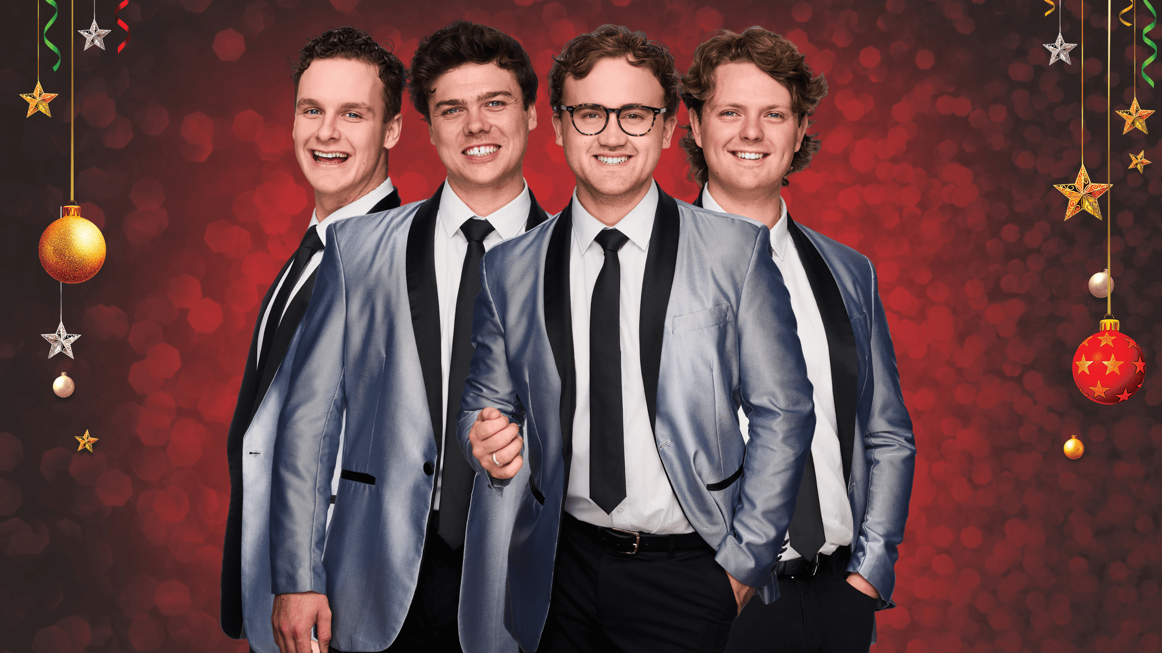 Four men in matching blue suits stand against a festive red background with ornaments.