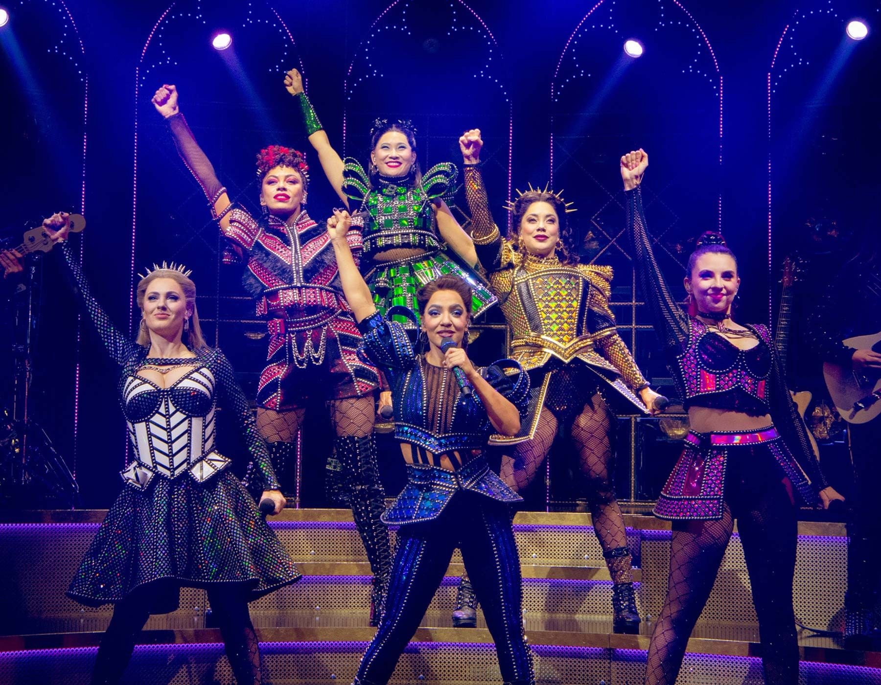 Six diverse female performers in queen-inspired outfits pose powerfully on a stage.
