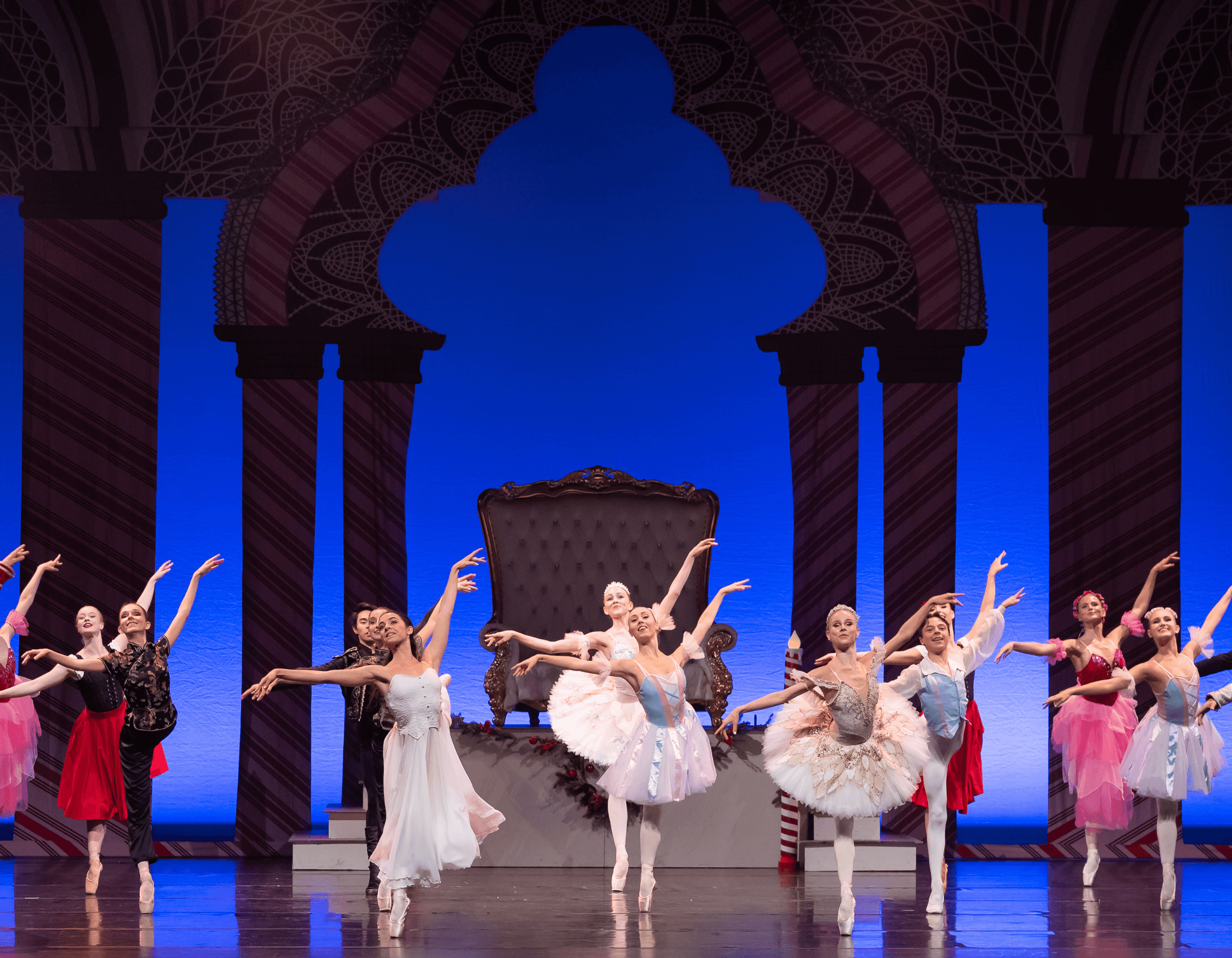 Ballet dancers in colorful costumes perform on an ornate stage with a blue backdrop.