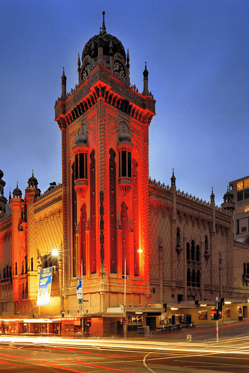 Historic building illuminated in vibrant red at night with car light trails.