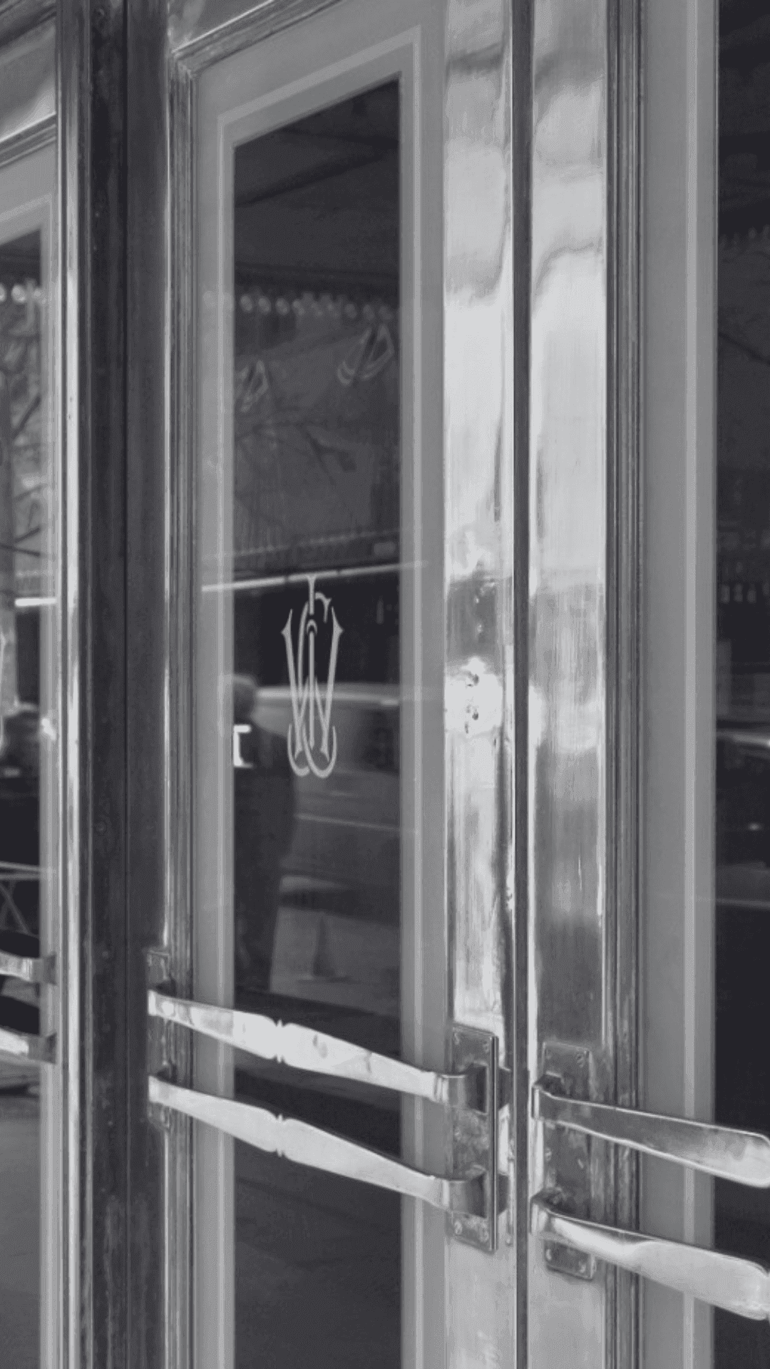 Black and white close-up of a glass door with a blurry reflection of a person.