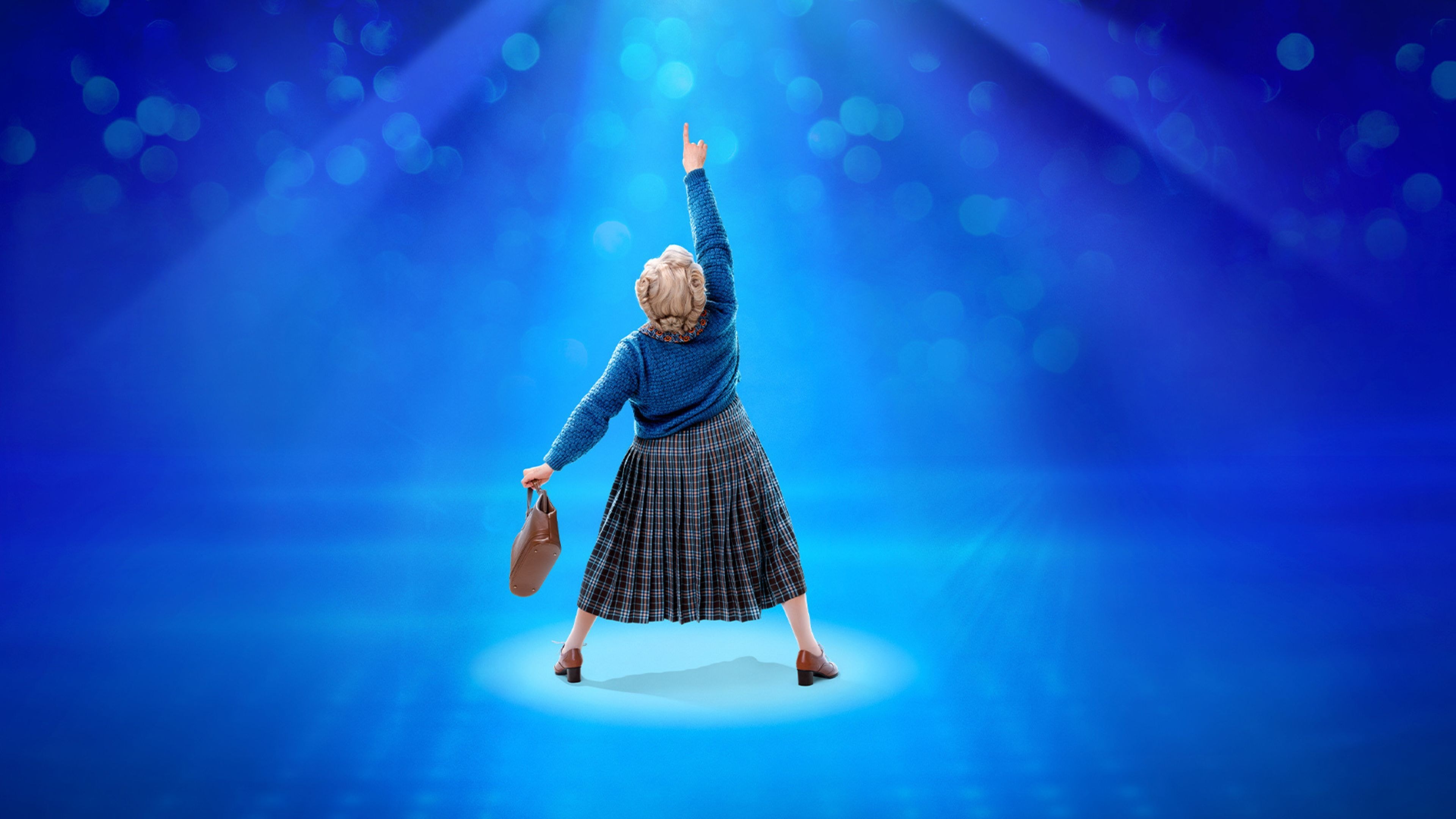 Woman in a blue sweater and plaid skirt points upwards on a spotlighted stage.