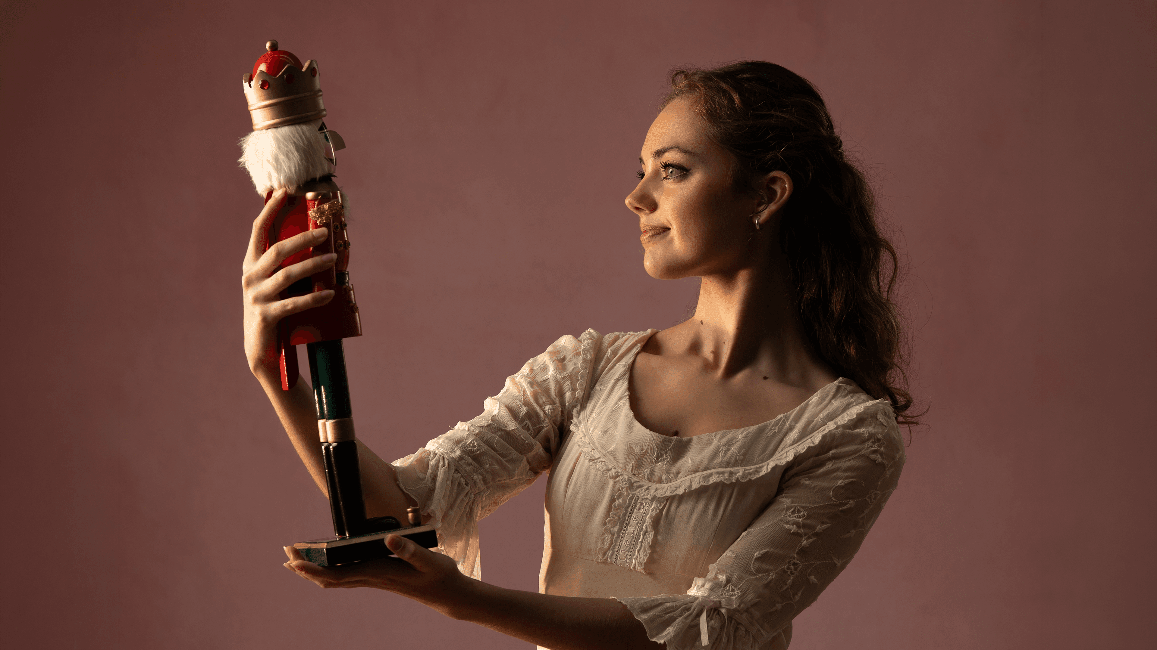 A ballerina in a white dress thoughtfully holds and gazes at a classic Nutcracker soldier.