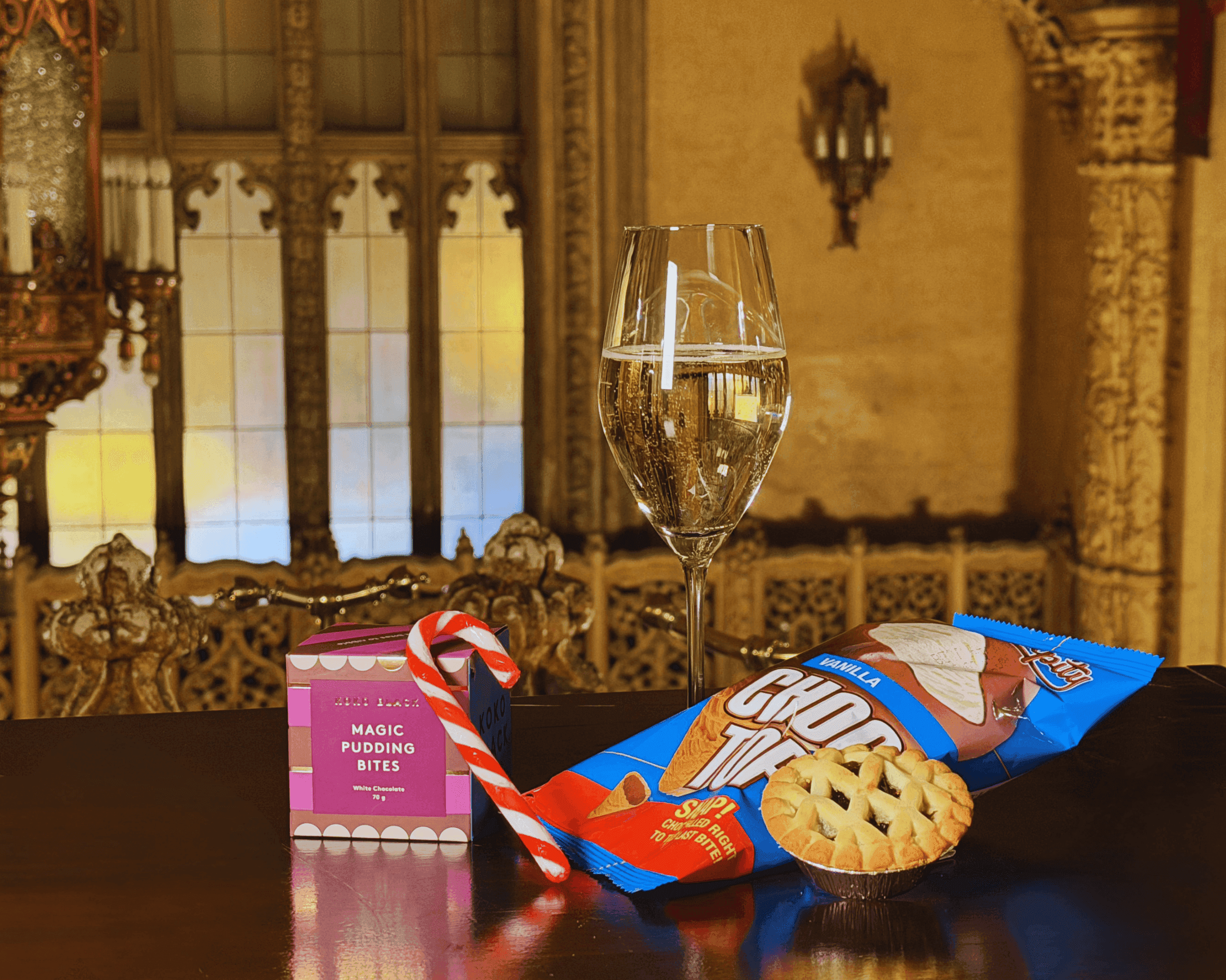 Champagne, cookies, candy cane, and snacks on an ornate table in a grand room.