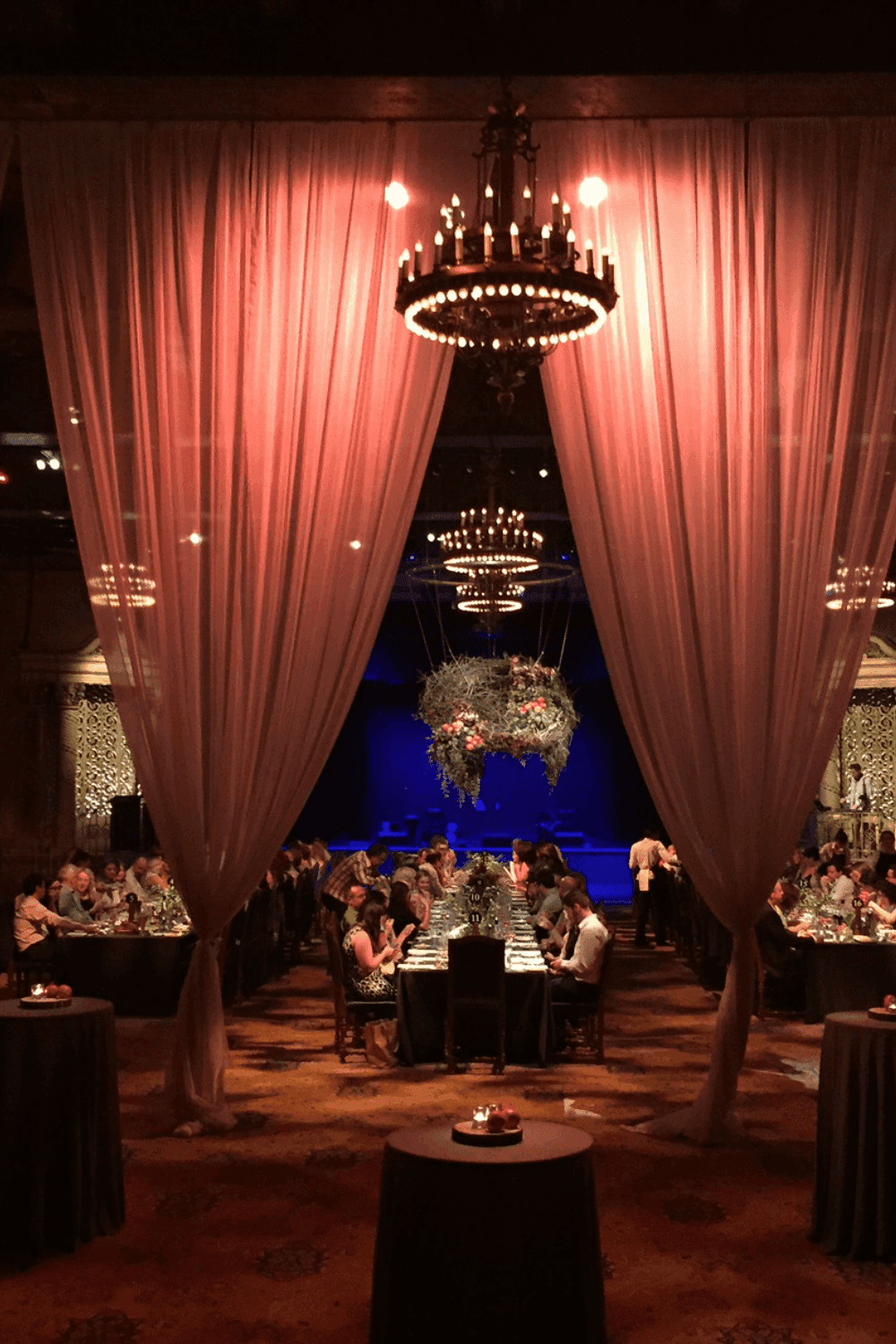 Elegant event hall with sheer pink drapes, chandeliers, and tables set for guests.