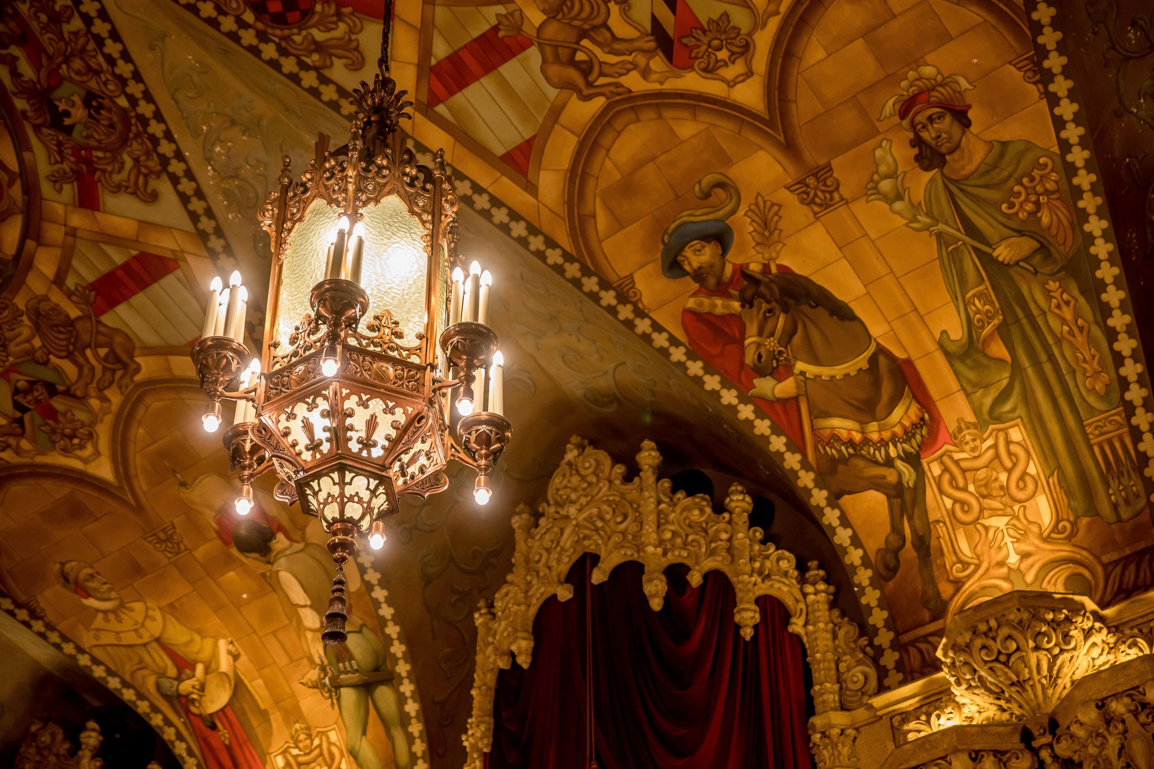Ornate ceiling murals and an illuminated chandelier in a grand, historic interior.