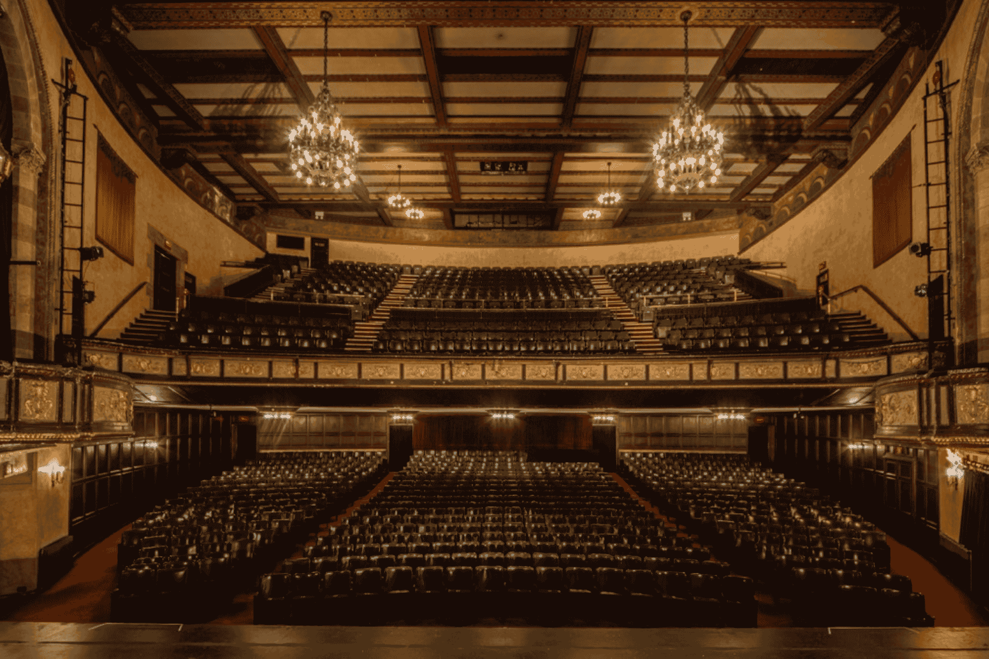 Empty grand theater with multiple levels of seating and elegant chandeliers.