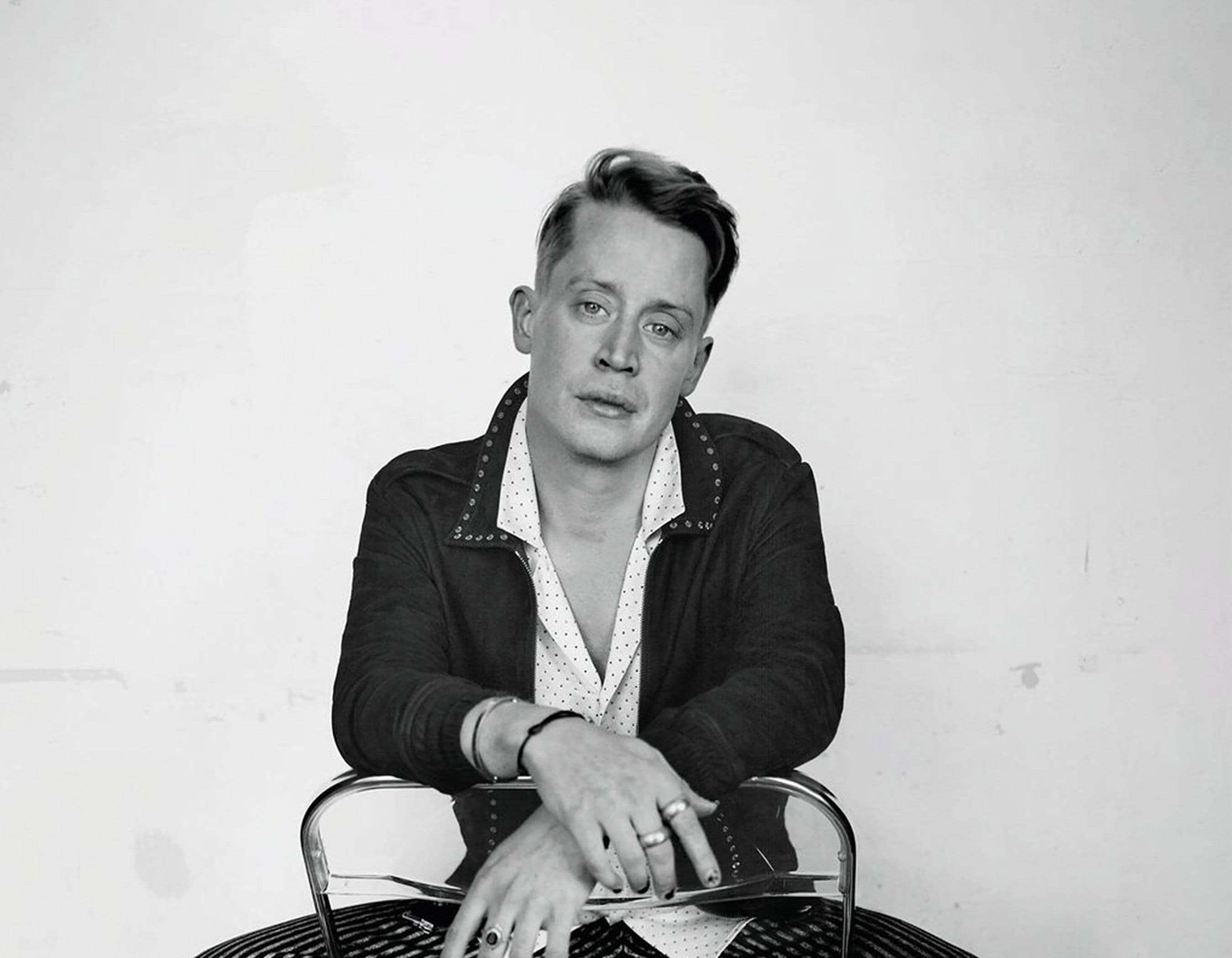 Black and white portrait of a man in a dark jacket, leaning on a chair.